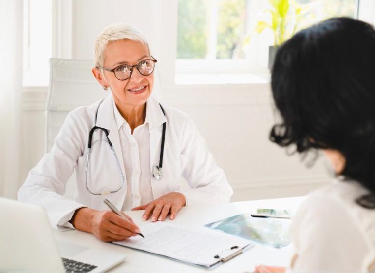 Un médecin avec un stéthoscope pendant un rendez-vous avec une patiente et l'écoute en souriant.